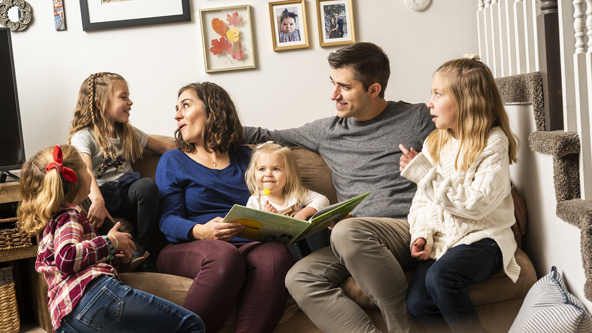 Family with four girls sit on couch reading a book