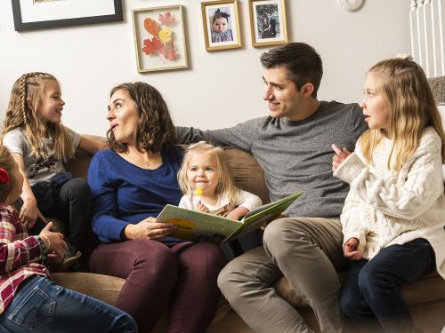 Family with four girls sit on couch reading a book