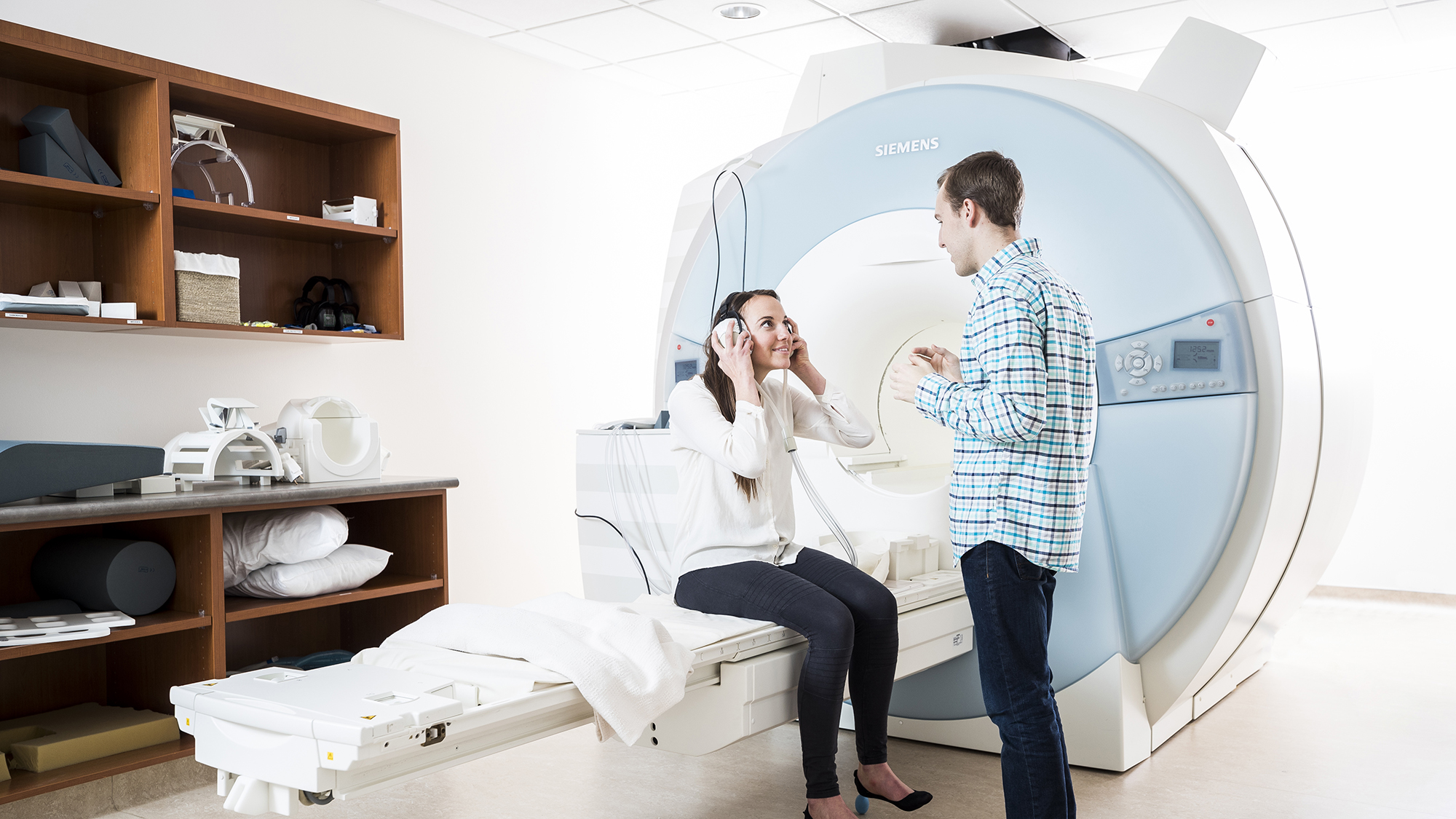 Female sits on an MRI bed talking with standing male