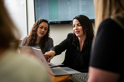 female using laptop conversing with another female