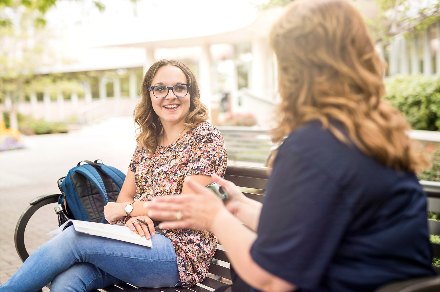 two women outside talking on a bench