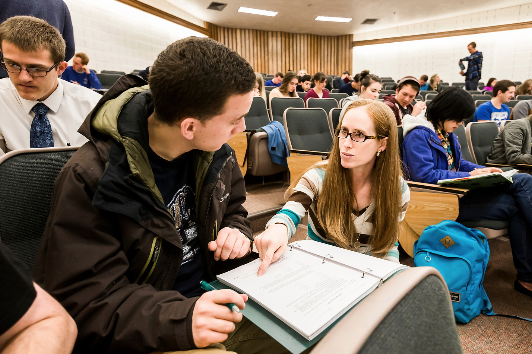 woman talking to male student in large classroom