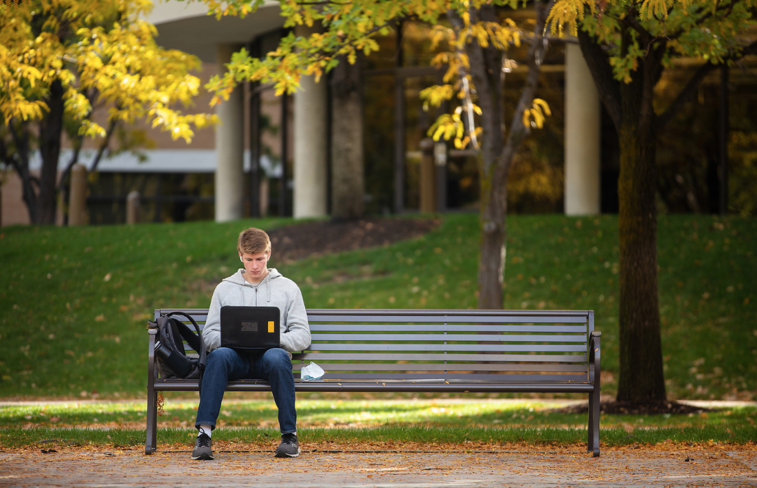 male sitting using laptop on outdoor bench